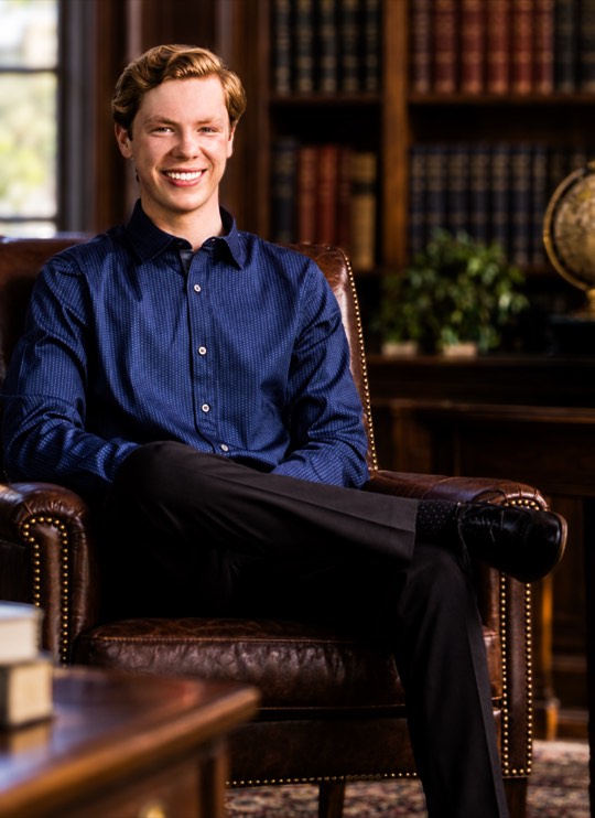 Alec Stevens, Head of School, seated in a leather armchair in a library